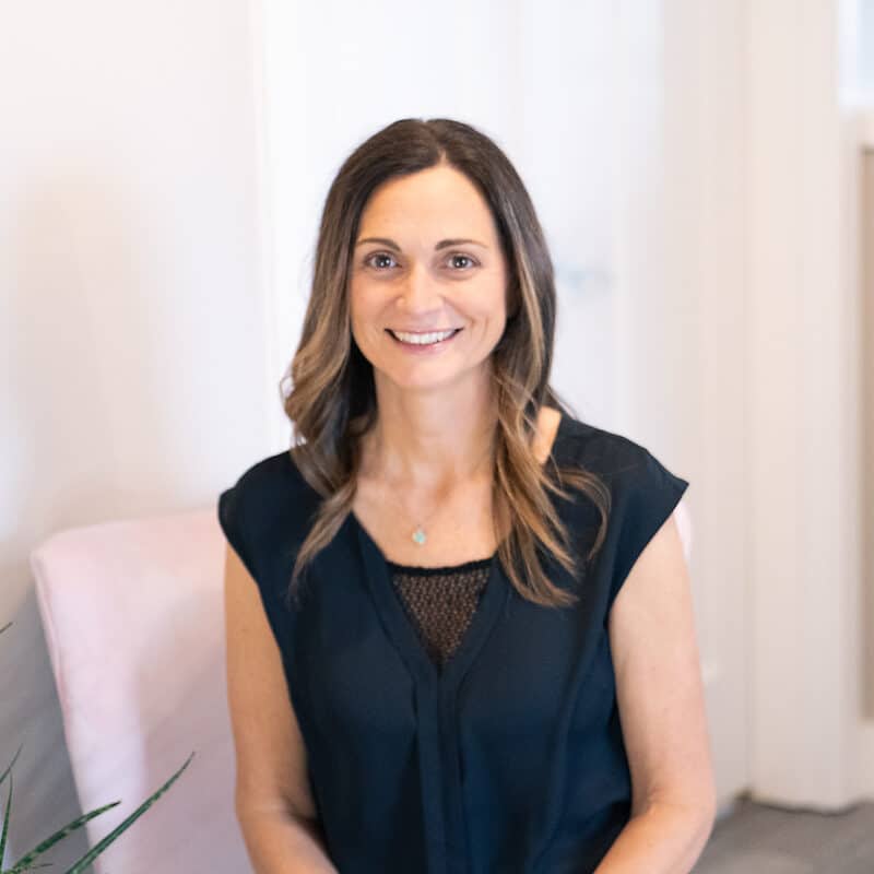 Alicia Lucero, smiling in a black blouse, seated indoors with soft lighting.